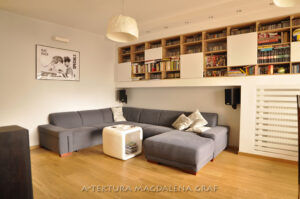 Salon z szarym narożnikiem i zabudową na książki i płyty